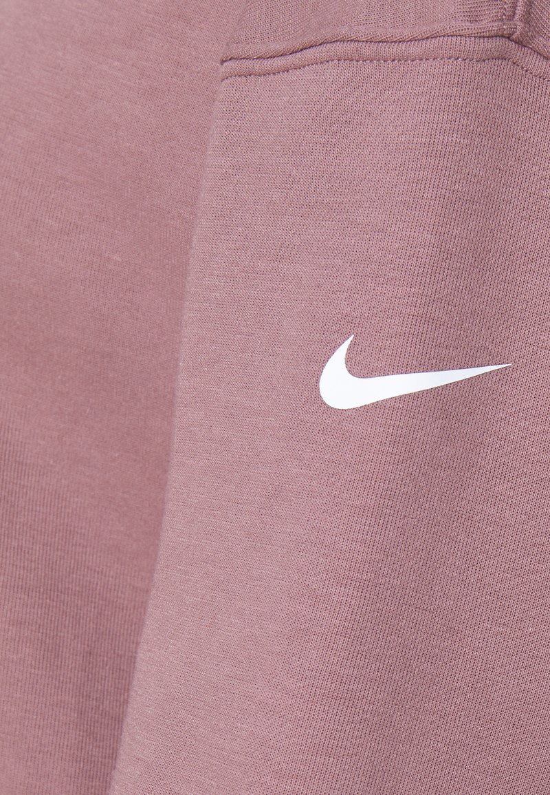 Lichtroze sweatshirt gemaakt van zachte stof, met een wit Nike-logo op de voorkant. De textuur lijkt glad en gebreid.