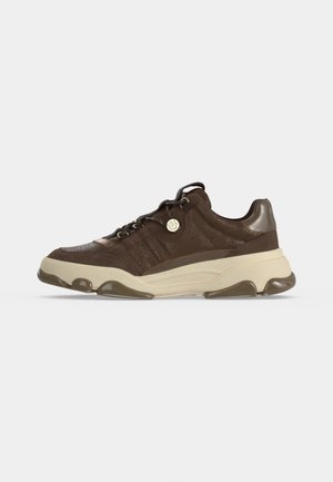 Brun ruskind lav sneaker med tyk beige sål, mørkebrune accenter, snørelukning og en rund metal logo ved siden.
