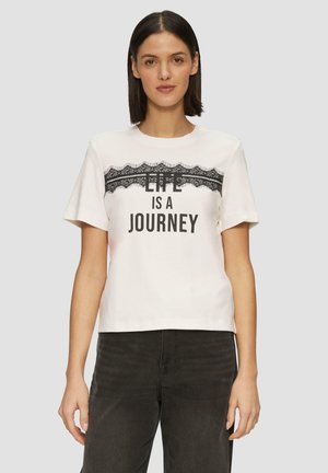 T-shirt en coton blanc à manches courtes et col rond, ornée de dentelle noire et portant le texte "LA VIE EST UN VOYAGE" en lettres en gras.