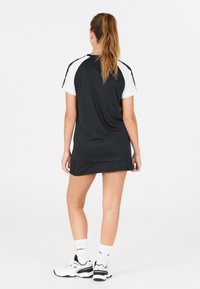 Svart träningströja med vita korta ärmar och rundad kant, matchad med en svart kjol. Modellen har på sig vita och svarta sneakers samt strumpor.