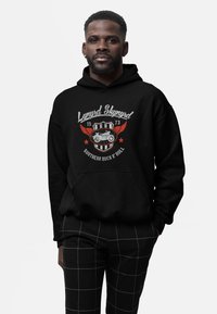 Sort hættebluse med "Lynyrd Skynyrd" logo, som har røde vinger, motorcykel grafik og grå bogstaver. Pullover stil med en frontlomme.
