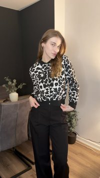 Svartvit leopardmönstrad stickad tröja med krage, matchad med svart högmidjade byxor; inomhusmiljö med växter i bakgrunden.
