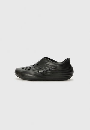 Chaussures à enfiler noires en plastique lisse avec un design à côtes, des trous perforés sur le dessus et un logo discret sur le côté.