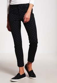 Černé patterned kalhoty s přiléhavým střihem a jemnými květinovými motivy, vyrobené z pružného materiálu, doplněné černými pohodlnými botami na zpevnění.