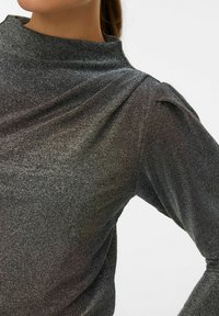 Juoda blizgi palaidinė su aukštu kaklu, ilgomis rankovėmis ir pūstais petukais, bei lygiu, tekstūruotu audiniu.