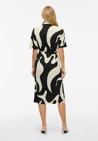 Svart och krämfärgad mönstrad midiklänning med korta ärmar, skjortkrage, knyt i midjan och slits baktill. Slät och lätt tygtextur.