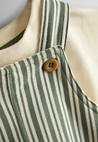 Zaļi un baltajiem vertikāli svītraina auduma gabals ar brūnu pogu ar četriem caurumiem, piešūtu pie siksnas pār krēmkrāsas adījumu.