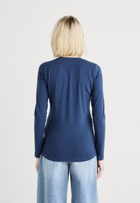 Langslieve marineblauw top van gladde stof, aansluitend ontwerp, ronde halslijn en iets gebogen zoom, gecombineerd met lichtblauwe wijde jeans.