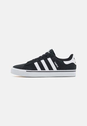 Zapatillas de ante negro con diseño de tres rayas blancas, suela blanca y acento en el talón de contraste. Estilo clásico con cordones y costuras simples.