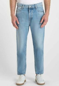 Jeans de denim azul claro con corte recto, que presentan un diseño estándar de cinco bolsillos y un ligero desgaste en la parte frontal, combinados con zapatillas blancas.