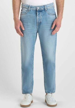 Jeans in denim azzurro chiaro con una linea dritta, caratterizzati da un classico design a cinque tasche e una leggera scoloritura frontale, abbinati a sneaker bianche.