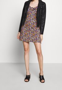 Czarna skórzana kurtka na kwiecistej mini sukience w fioletowe, pomarańczowe i różowe kwiaty. Modelka ma na sobie czarne sandały na obcasie z ćwiekami.