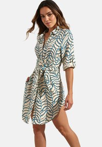Shirtjurk in lichtbeige met een blauw golfpatroon, voorzien van een kraag, knoopsluiting, opgerolde mouwen en een strikdetail in de taille.