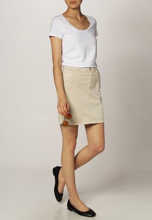 Jupe en denim beige avec une coupe droite et des poches avant, associée à un haut à manches courtes blanc. Les accessoires incluent des lunettes de soleil rondes.