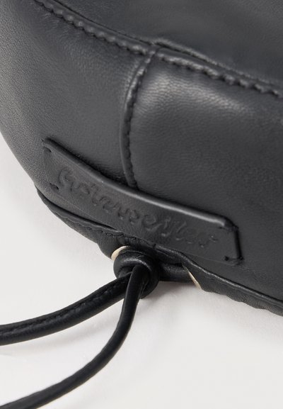 Κοντινό πλάνο γωνίας μαύρης δερμάτινης τσάντας με ραμμένες ραφές, κεντημένη ετικέτα μάρκας και κορδόνι με κορδόνι δεμένο σε κόμπο.
