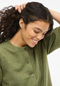 Oliwkowo-zielony kardigan z okrągłym dekoltem, dwoma guzikami z przodu i miękkim, teksturowanym splotem. Tkanina wygląda na przytulną i ciepłą.