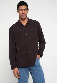 Sötétlila, hosszú ujjú ing hegyes gallérral, két első zsebbel és gombokkal. Kapcsolatlanul viselve kék farmer felett.