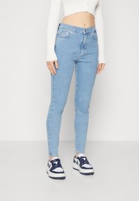 Jeans ajustados de color azul claro fabricados en denim, con una cintura de altura media, cinco bolsillos y un acabado limpio en los tobillos, combinados con zapatillas blancas.