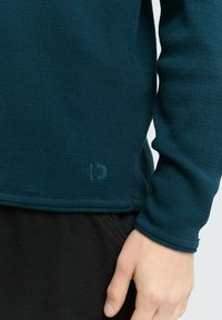Donkergroen, geweven longsleeve shirt met een ronde halslijn en een logodetail nabij de zoom, gecombineerd met zwarte stof.