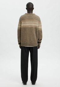 Pull marron texturé avec col rond, présentant des rayures horizontales plus claires. Associé à un pantalon noir ample.