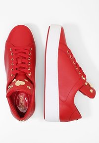 Baskets en cuir rouge avec une semelle extérieure blanche, ornées d'accents en forme de cœur dorés et d'un design à lacets. Texture lisse et forme arrondie à l'avant.