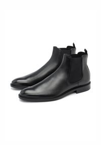 Botines Chelsea de cuero negro con paneles elásticos laterales, punta redondeada, diseño elegante y suela de goma plana. Cuenta con tiradores para facilitar el calzado.