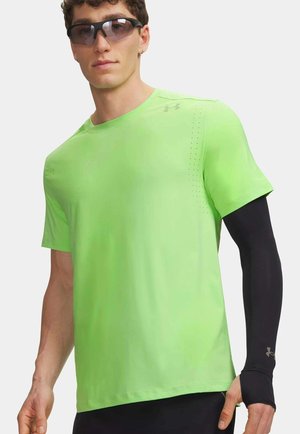 Uomo che indossa una maglietta sportiva a maniche corte verde neon, manicotto nero per il braccio e occhiali da sole neri, in piedi contro uno sfondo bianco.