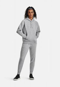 Sweatshirt cinzento com capuz, cordão e bolsos frontais, combinado com calças de treino a condizer. Ambos os artigos têm uma textura suave e punhos elásticos.