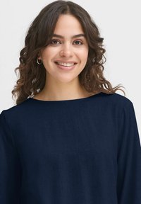 Maglietta a maniche lunghe blu navy con scollatura ampia. Texture liscia, design minimalista e morbido tessuto visibile nell'aspetto del capo.