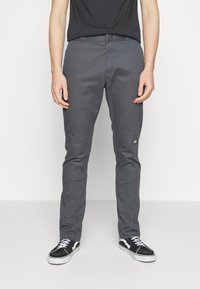 Szare spodnie o slim fit, z przednimi kieszeniami, subtelnym logo na lewej udzie, połączone z czarno-białymi sneakersami.