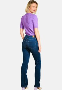 Ozke modre kavbojke iz jeansa z visokim pasom, zadnjimi žepi in usnjeno etiketo. Kombinirane s kratkoročno lila majico.