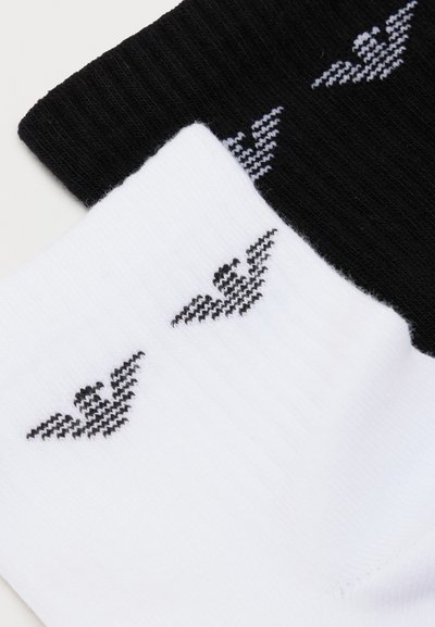 Chaussettes côtelées noires et blanches avec de petits logos d'aigle ailé tricotés près du bord supérieur de chaque paire.