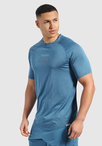 Niebieska koszulka sportowa wykonana z teksturowanej tkaniny, z okrągłym dekoltem, krótkimi rękawami oraz subtelnym logo marki na klatce piersiowej.