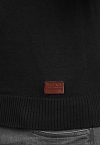 Maglione nero a maglia con orlo a coste, caratterizzato da un'etichetta in pelle marrone con la scritta "BLEND" cucita nella parte inferiore davanti.
