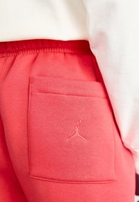 Pantalon de survêtement rouge avec taille élastique et poche arrière affichant un logo Jumpman subtilement brodé, porté avec un haut blanc.