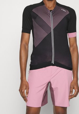 Czarny krótki rowerowy dżersej z różowymi geometrycznymi liniami i przednim zamkiem błyskawicznym, w połączeniu z jasnoróżowymi rowerowymi szortami.