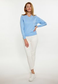  Lichtblauwe V-hals trui met lange mouwen, gecombineerd met aansluitende witte broek en witte sneakers. Gladde textuur met een relaxte pasvorm.