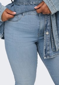 Χέρια που προσαρμόζουν τη μέση των ανοιχτό μπλε τζιν, φορόντας τζιν μπουφάν που ταιριάζει με κουμπιά και ραφές λεπτομέρειες.