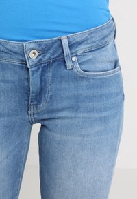 Jeans de mezclilla azul claro con un diseño ajustado, que cuentan con un cierre de botón en la parte frontal, cinturilla y bolsillos laterales. Textura suave y con una elasticidad moderada.