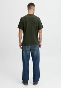 Olijfgroene t-shirt met korte mouwen en een relaxte pasvorm, gecombineerd met lichtblauwe losse denim jeans en bruine schoenen. Eenvoudig ontwerp, geen patronen.