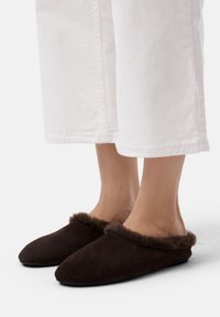 Braune Wildlederschlüpfschuhe mit einem weichen, pelzigen Besatz am Kragen. Das Design ist als Slipper mit einer abgerundeten Zehenpartie und einer flachen Sohle gestaltet.
