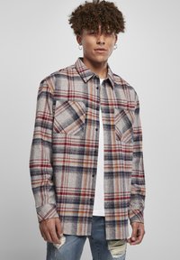 Rutig skjorta i grått, rött och marinblått, gjord av textilerad väv. Har två bröstfickor och krage. Bärs över en vit t-shirt.