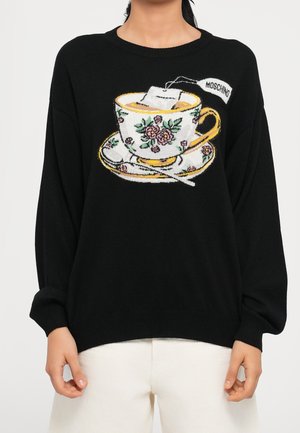Pull noir avec un motif floral de tasse à thé, soucoupe et cuillère, incluant une étiquette de sachet de thé portant la mention Moschino sur la poitrine.