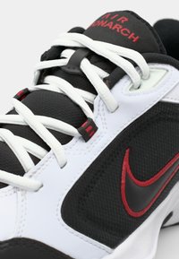 Tenisii alb-negru au accente roșii, țesătură texturată și șireturi. Logo-ul Nike este vizibil pe limbă și pe lateral.