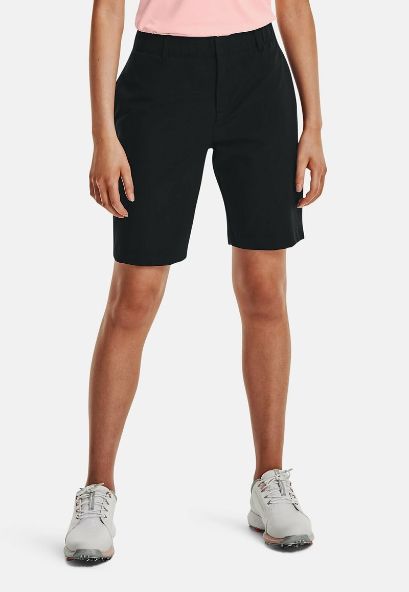 Svarta knälånga shorts med flat front, elastisk midja och en slät textur. Matchas med vita sportskor.