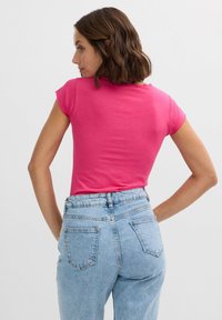 Camiseta ajustada rosa de manga corta, con textura suave y escote redondo. Combinada con vaqueros de mezclilla azul claro de tiro alto con bolsillos traseros.