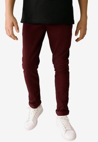 Pantalon slim fit bordeaux en coton, avec une texture lisse et des ourlets reversés, assorti à des baskets blanches.