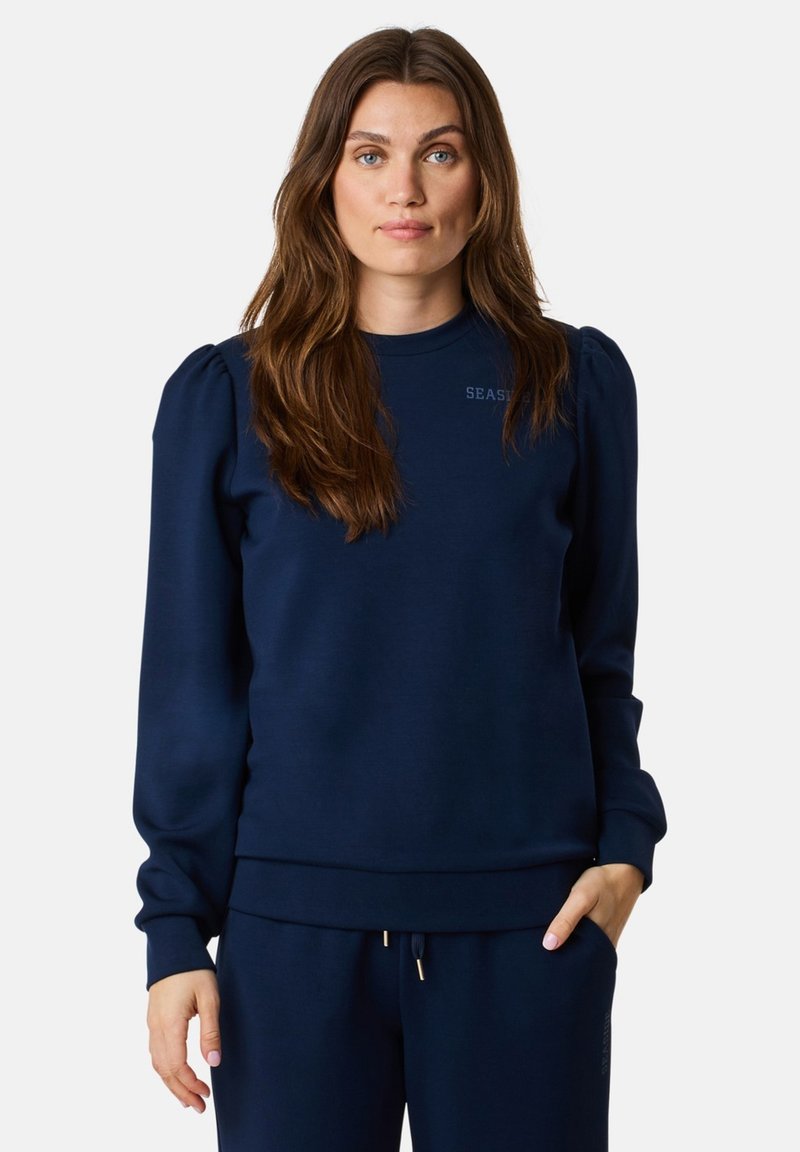 Felpa blu navy con maniche a palloncino e orlo a coste. Presenta un logo ricamato "SEAS" sul petto, abbinata a pantaloni jogger coordinati.