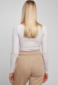 Langermet, tettsittende hvit topp med en jevn tekstur. Sammen med beige, høytlivsbukser med en myk midje og lommer.