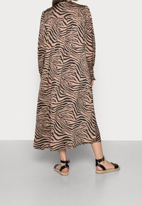 Lång, flödande klänning med en beige bakgrund och svarta zebraränder, med långa ärmar och en avslappnad siluett. Svarta sandaletter med remmar.